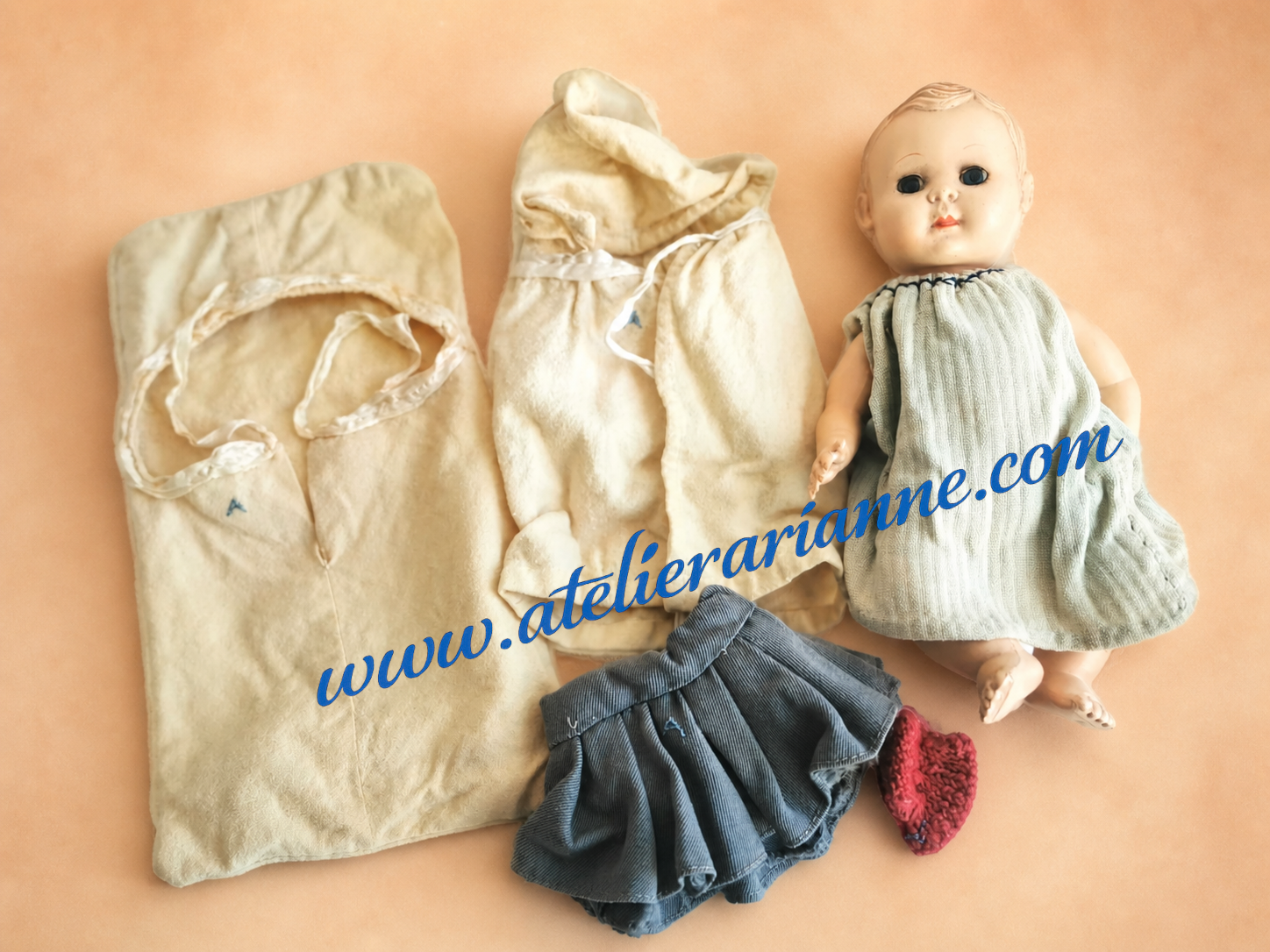 Poupon ancien avec vêtements, couffin et petits habits, issu d’un don de poupées anciennes au musée Atelier Arianne.