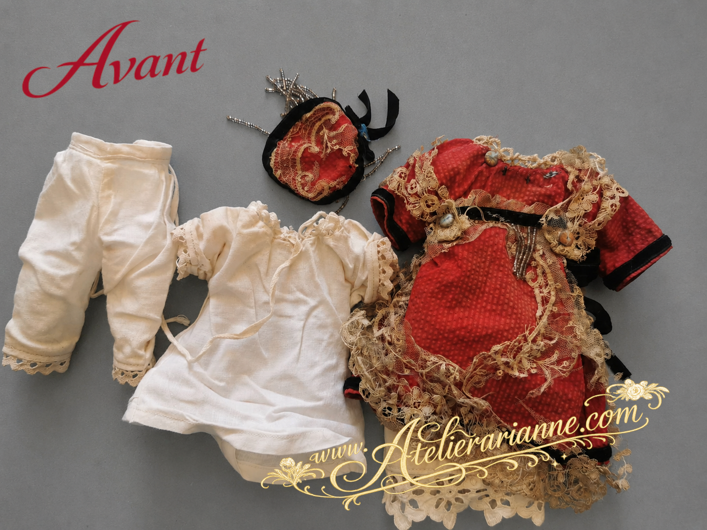 Ensemble de vêtements anciens de poupée mignonette avant restauration, avec robe rouge, coiffe assortie, sous-vêtements blancs, dentelle ancienne abîmée et détails décoratifs fragilisés.