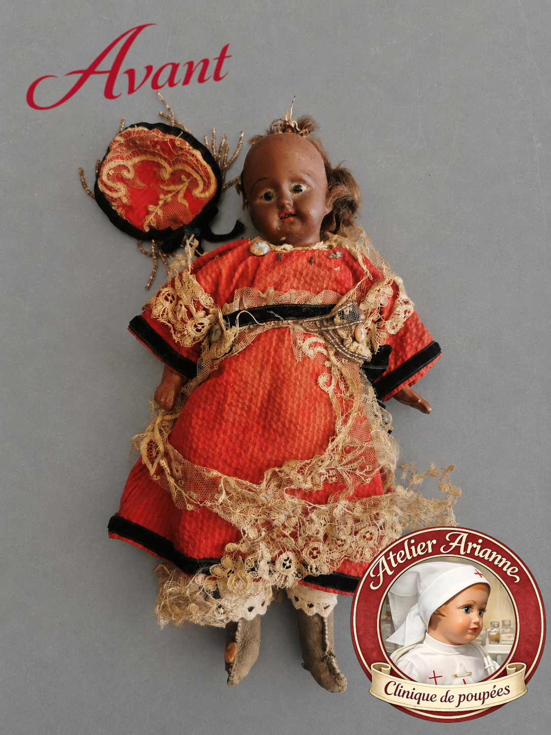 Poupée mignonette avant restauration, portant une tenue ancienne rouge très abîmée, avec coiffe assortie, dentelle déchirée, perles décoratives et détails fragilisés.