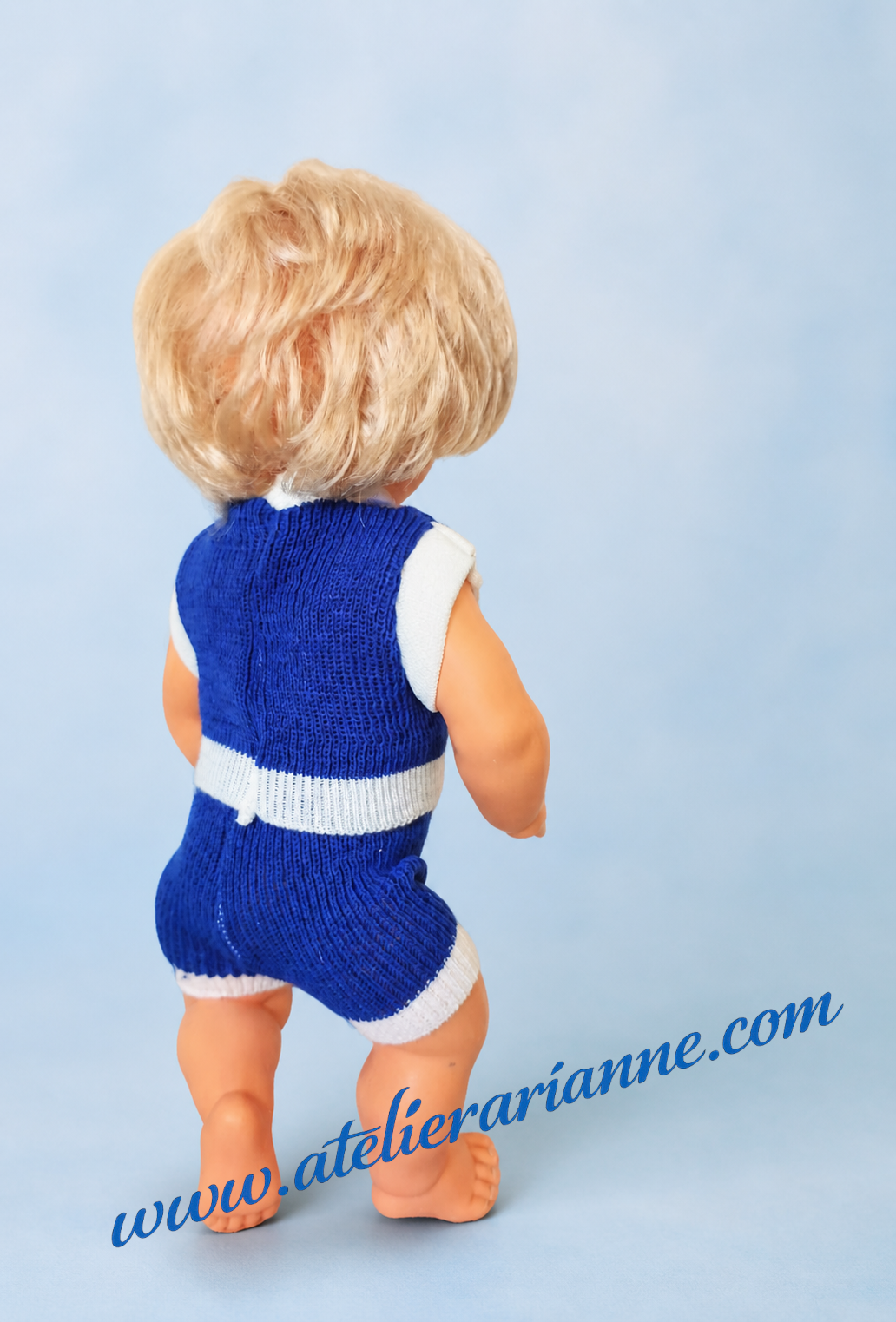 Dos du poupon Arnaud Petitcollin apr&egrave;s remise en beaut&eacute;, avec cheveux blonds implant&eacute;s et tenue bleue et blanche.