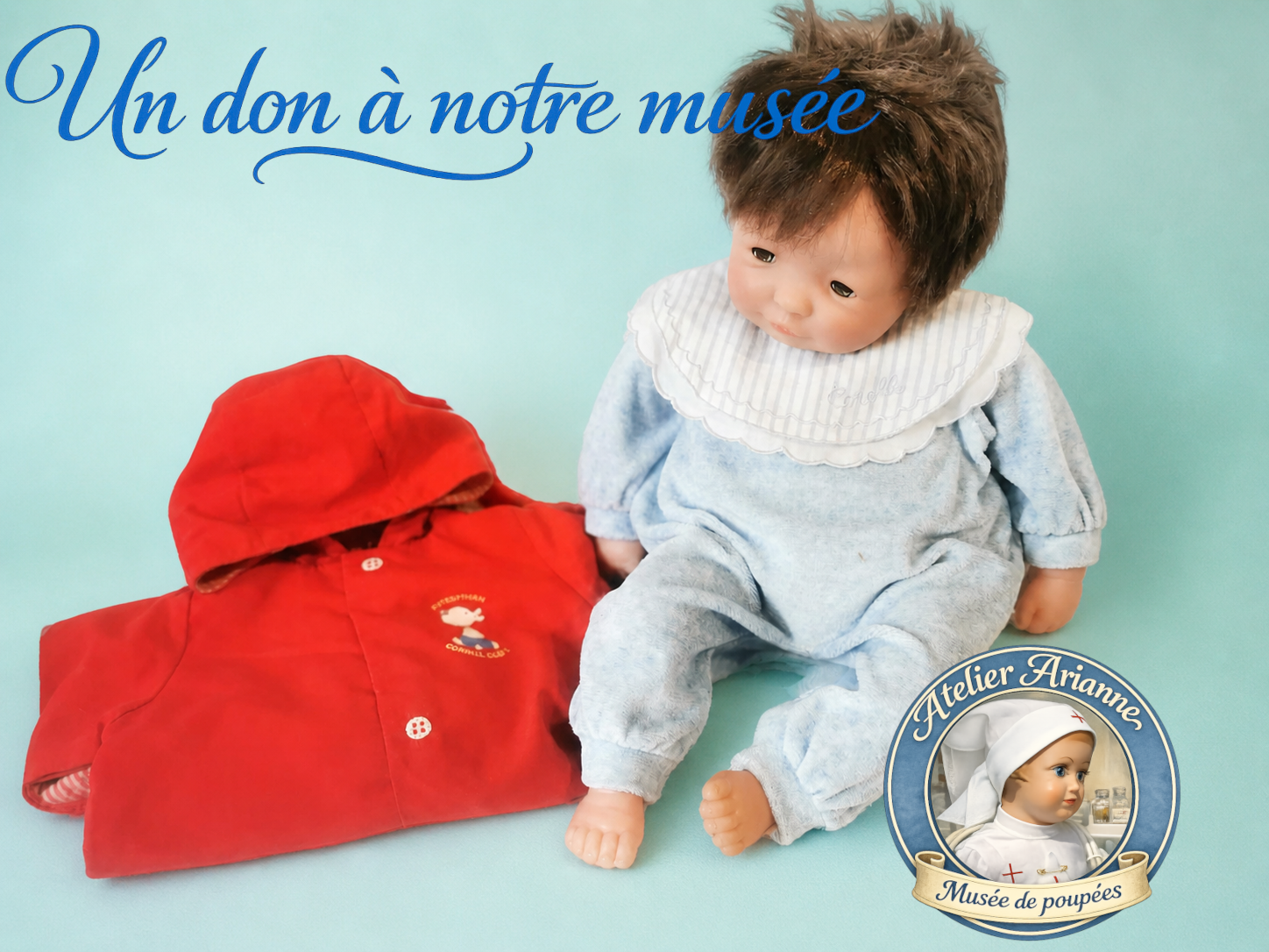 Photo d&rsquo;un b&eacute;b&eacute; Corolle accompagn&eacute; d&rsquo;un manteau rouge, don confi&eacute; au mus&eacute;e Atelier Arianne pour enrichir la collection de poup&eacute;es, v&ecirc;tements et souvenirs d&rsquo;enfance.