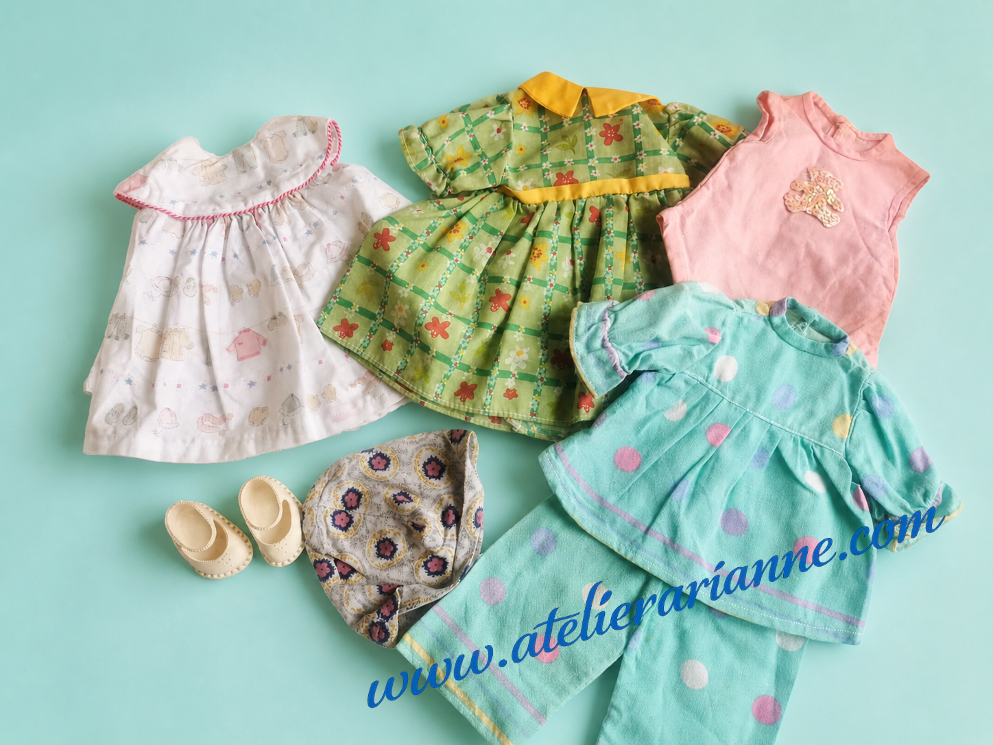 Photo de plusieurs v&ecirc;tements de poup&eacute;es donn&eacute;s au mus&eacute;e Atelier Arianne : robes, ensemble vert fleuri, tenue rose, v&ecirc;tement bleu &agrave; pois, petit bonnet et chaussures, pour documenter les habits et accessoires de poup&eacute;es d&rsquo;enfance.