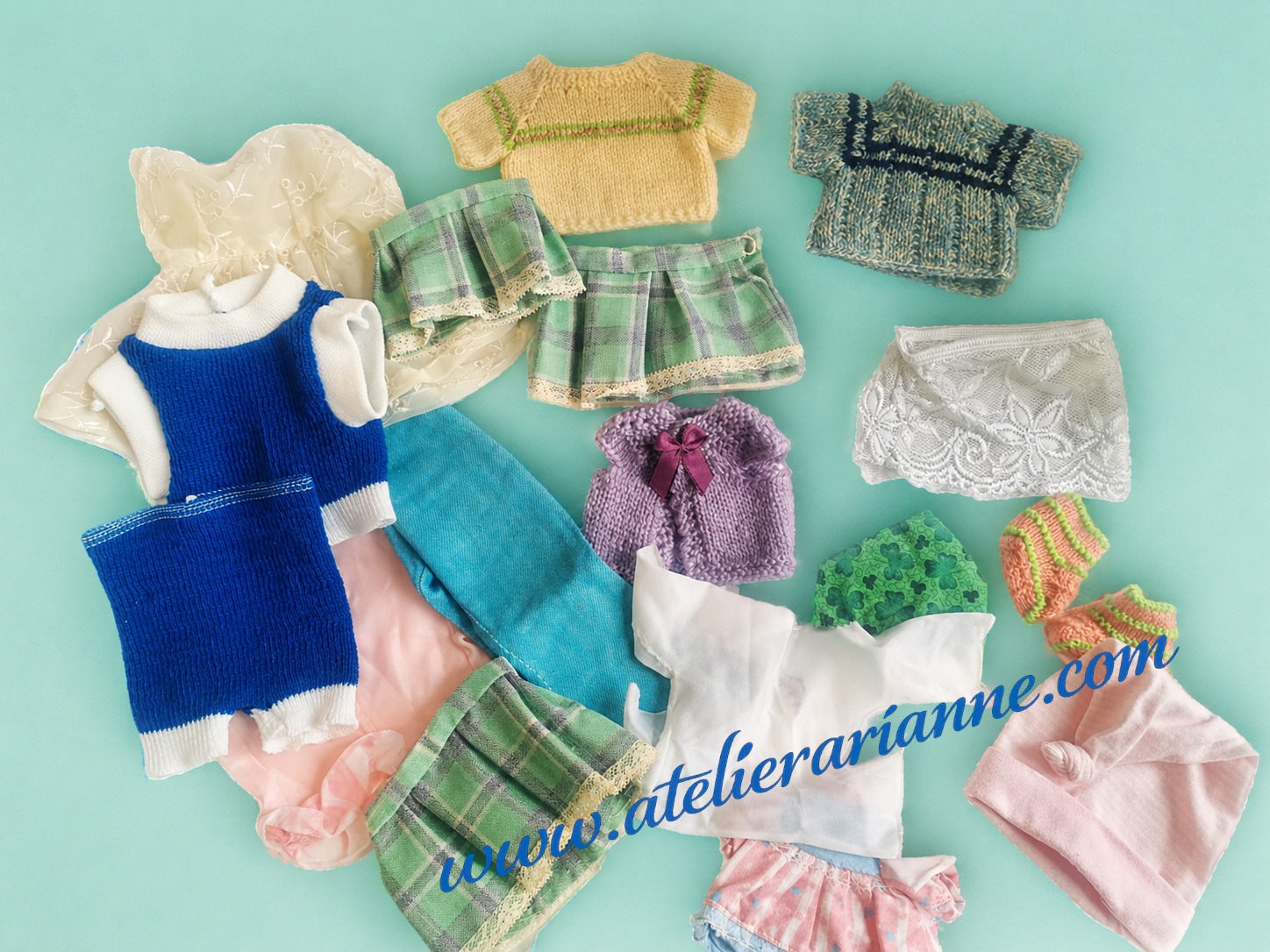 Photo d&rsquo;un ensemble de v&ecirc;tements de poup&eacute;es donn&eacute;s au mus&eacute;e Atelier Arianne : robes, tricots, petits bonnets et accessoires textiles destin&eacute;s &agrave; enrichir la documentation sur les poup&eacute;es et souvenirs d&rsquo;enfance.