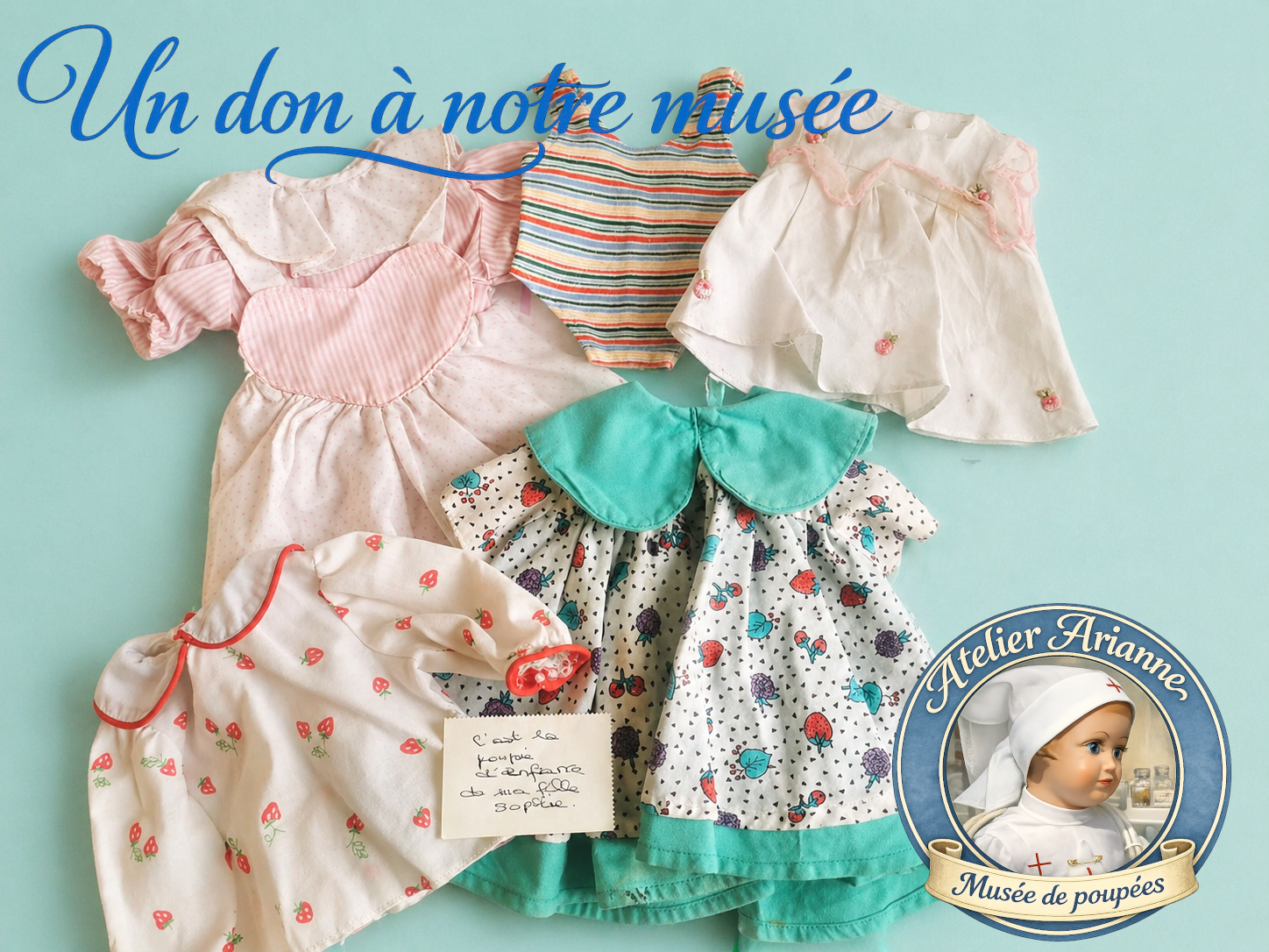 Photo de robes et v&ecirc;tements de poup&eacute;es donn&eacute;s au mus&eacute;e Atelier Arianne, avec plusieurs tenues en tissu, une robe &agrave; col vert, une tenue ray&eacute;e et une note manuscrite conserv&eacute;e pour documenter les souvenirs d&rsquo;enfance.