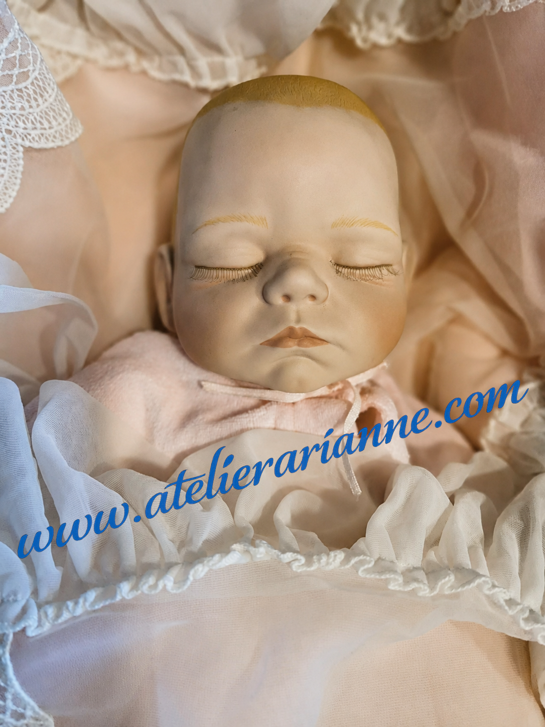 Ce gros plan montre toute la douceur de ce b&eacute;b&eacute; de collection, probablement Ashton-Drake, &agrave; confirmer apr&egrave;s observation compl&egrave;te.

Son visage endormi, sa t&ecirc;te en porcelaine, son corps en tissu et sa layette d&eacute;licate lui donnent une pr&eacute;sence tr&egrave;s touchante. Avec sa pr&eacute;sentation de naissance, sa couverture et son petit bracelet, elle &eacute;voque ces poup&eacute;es pens&eacute;es comme de v&eacute;ritables b&eacute;b&eacute;s &agrave; ch&eacute;rir.

C&rsquo;est un ensemble tr&egrave;s &eacute;mouvant pour le mus&eacute;e, car il ne montre pas seulement une poup&eacute;e, mais tout un univers de tendresse, de soin et de souvenirs autour du b&eacute;b&eacute;.

Doroth&eacute;e &ndash; Atelier Arianne &ndash; clinique et mus&eacute;e de poup&eacute;es 