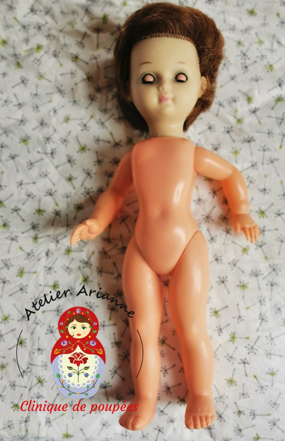 Petite poup&eacute;e Bella avant restauration, allong&eacute;e sur un tissu, avec le vinyle jauni par le temps et les yeux ferm&eacute;s avant les travaux de remise en &eacute;tat pour le mus&eacute;e Atelier Arianne.