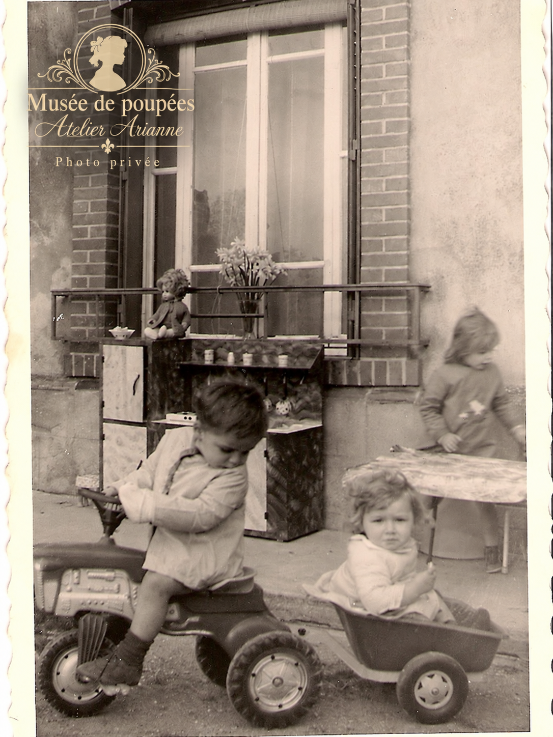 Trois enfants jouant avec un tricycle, une remorque et du mobilier miniature ancien